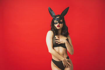 Image of a woman wearing a sexy rabbit mask and posing on a red colored background - obrazy, fototapety, plakaty