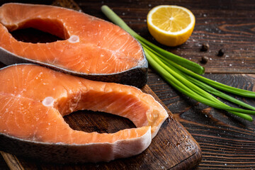 Two fresh red fish steaks (salmon or trout) on dark wooden background.