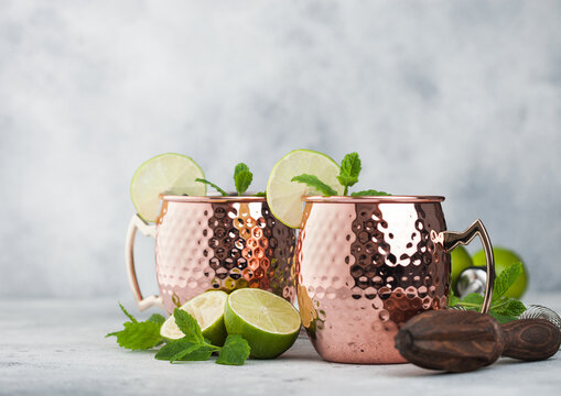 Moscow mule cocktail in a copper mug with lime and mint and wooden squeezer on light background