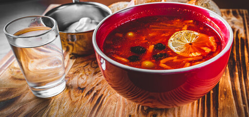 Solyanka soup with meat, sausage, vegetables, olives and lemon in bowl on wooden table background