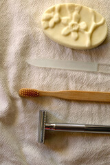 Sustainable toiletries on linen cloth: reusable metal safety razor, wooden toothbrush, glass nail file and soap bar. Top view.