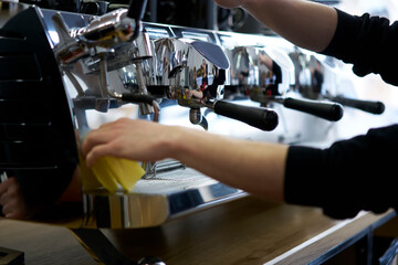 Cropped image of female hands cleaning professional metal machine for aroma coffee making, woman barista checking italian equipment at bar for preparing hot beverages and orders at cafeteria