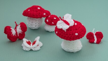 Obraz na płótnie Canvas Crochet mushroom and butterfly in red and white strains of yarn as martenitsa, Bulgarian folklore tradition with adornment symbols for spring in march. Shallow depth of focus, light green background.