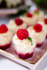 Single serving mousse desserts on a candy bar of a wedding banquet. Catering, festive buffet. Tasty mousse dessert with jelly and berries in a glass on light background close up. Delicious dessert