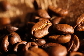 Macro closeup of pile fresh roasted organic coffee beans on jute fabric sack (focus on center)
