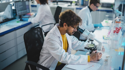 Medical Science Laboratory: Handsome Latin Scientist Looking Under Microscope to Analyse New...