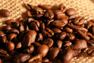 Macro closeup of pile fresh roasted organic coffee beans on jute fabric sack (focus on center)