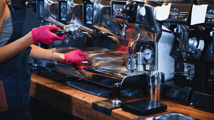 cropped view of barista holding portafilter near professional coffee machine