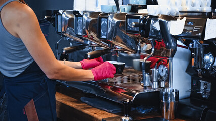 partial view of barista holding cups near modern coffee machine in coffee shop