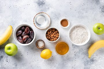 Obraz na płótnie Canvas various ingredients for vegan baking: buckwheat flour, dates, bananas, almonds, honey, coconut oil. Gray background. top view. copy space