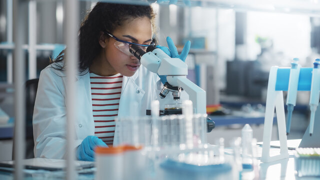 Medical Science Laboratory: Portrait of Beautiful Black Scientist Looking Under Microscope Does Analysis of Test Sample. Ambitious Young Biotechnology Specialist, working with Advanced Equipment