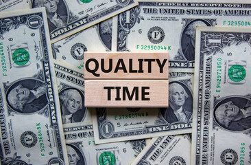 Quality time symbol. Wooden blocks with words 'quality time'. Beautiful background from dollar bills. Business and quality time concept. Copy space.