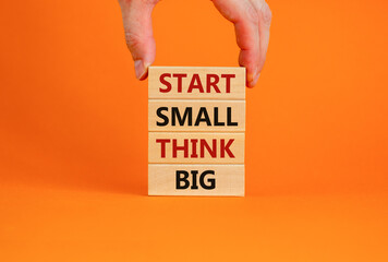 Start small think big symbol. Concept words 'Start small think big' on wooden blocks on a beautiful orange background. Businessman hand. Business, motivational and start small think big concept.