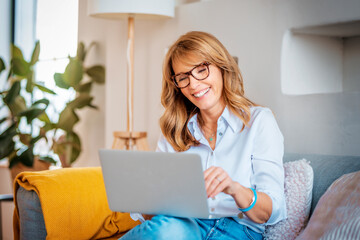 Happy mature woman using laptop while sitting on the couch at home