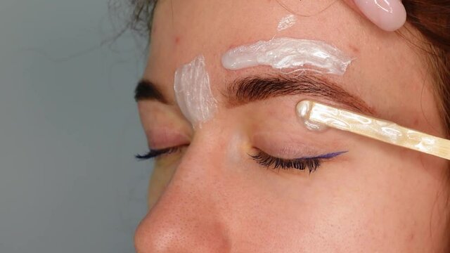 Brow master applying hot wax for brows epilation, lamination and waxing. Professional care for face and brow beauty procedures. 
