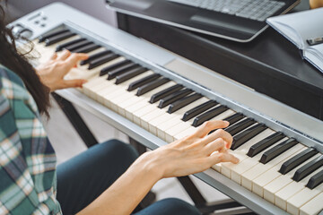 Fototapeta na wymiar Close up of unrecognizable young woman playing electric piano teaching remotely using laptop while working from home. Online education and leisure concept.