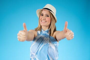 Obraz na płótnie Canvas Smiling pretty young woman in summer clothes showing thumbs up isolated over blue background