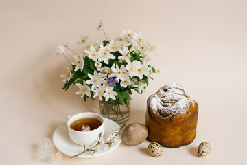 Easter cake craft in. Craft with raisins, candied fruits and a sprinkle of powdered sugar. Homemade cake. Eggs, a cup of tea and spring flowers in a vase on a beige background