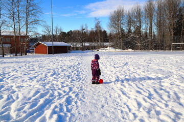 Stockholm, Sweden. February 06, 2021. A kid playing outside in the snow with a pink football....