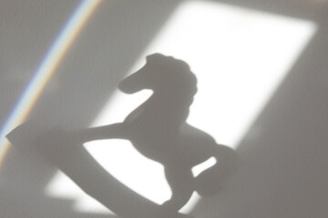 The rocking toy horse casts the shadow on a wall of the room. Childhood concept.