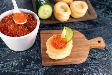 Recipe for making an appetizer with red caviar. Tartlets, red caviar, cucumber on a black background. Cooking process.
