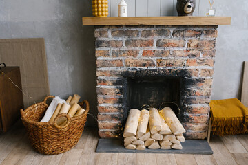 Scandinavian interior with red brick fireplace, wicker basket for firewood, pile of logs for a fire