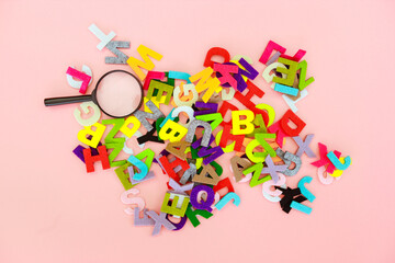 A magnifying glass with the colorful alphabet on pink background. Education concept.