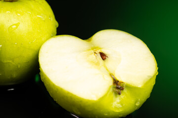 whole green apple and cut in half with splash and flow of water on dark background