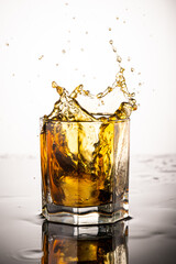 splash in glass with whiskey from falling ice on white background