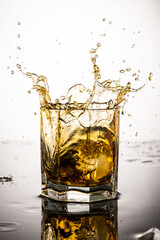 splash in glass with whiskey from falling ice on white background