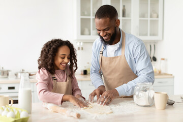 Obraz na płótnie Canvas Happy black man and his child daughter kneading dough