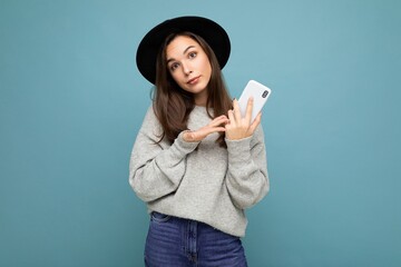 Beautiful young asking dissatisfied brunette woman wearing black hat and grey sweater holding...