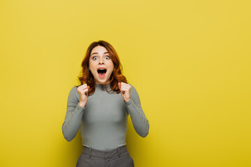 excited young woman with clenched fists looking at camera on yellow