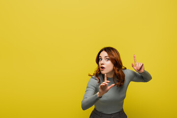 woman with curly hair and open mouth pointing with fingers isolated on yellow