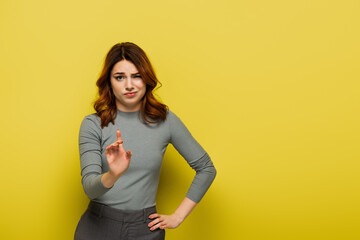 displeased woman standing with hand on hip and pointing with finger while showing no sign on yellow - obrazy, fototapety, plakaty