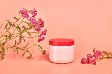 pink jar without inscriptions. against the background of red flower yarrow. concept cosmetics skin care