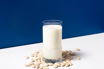 Vaso de leche vegetal de almendras con almendras naturales blancas sobre mesa blanca y fondo azul