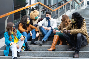 group of millennials on a staircase in the city smiling and talking while wearing face masks, group...