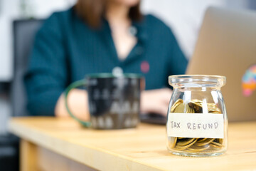 tax refund concept with gold coin in bottle with soft focus woman use laptop background