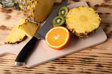 Juicy pineapple and kiwi cut in half with chefs knife on a wooden cutting board
