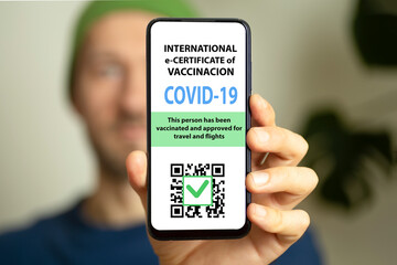The men is holding a smartphone with electronic coronavirus vaccination certificate or vaccine passport for travellers. COVID-19 immunity e-passport mobile app for international travelling