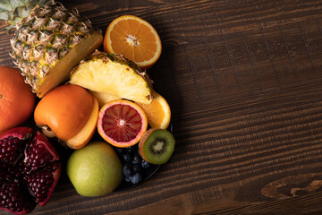 Naklejka na ściany i meble Selection of sliced fresh fruits with kiwis and blood orange on a plate on wooden background with free text space