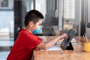 Young Asian man student studying online at home with a tablet. Wear a mask.