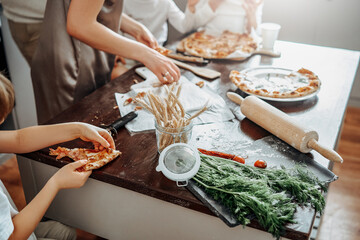 Atmospheric portrait of a happy family in modern kitchen. Mother cooking pizza and her children taste and eat sitting at table.