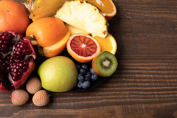 Naklejka na ściany i meble Selection of sliced fresh fruits with kiwis and blood orange on a plate on wooden background with free text space