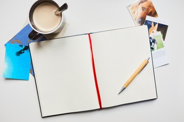 A beautiful notebook surrounded by a classical camera, some photos, a postcard, a pen and a coffee.