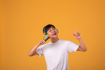 Happy young Asian man wearing headphones listening to music on mobile phone on orange background.