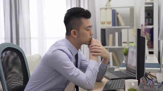 asian manager facing challenge in project planning is staring at computer screen and thinking hard with hands clasped under chin