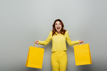 astonished woman in yellow clothes holding shopping bags on grey