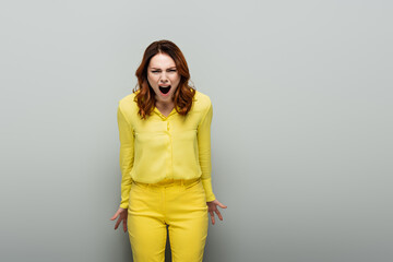 angry woman in yellow clothes yelling while looking at camera on grey